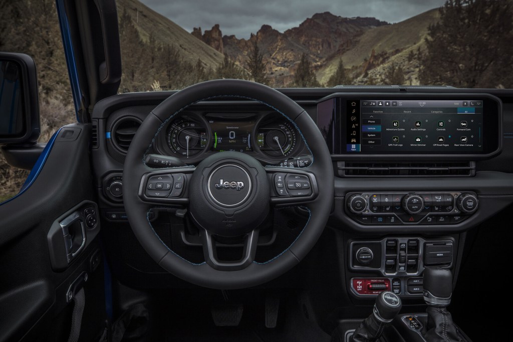 Jeep Wrangler steering wheel and digital gauge cluster with a mountain trail visible through the windshield